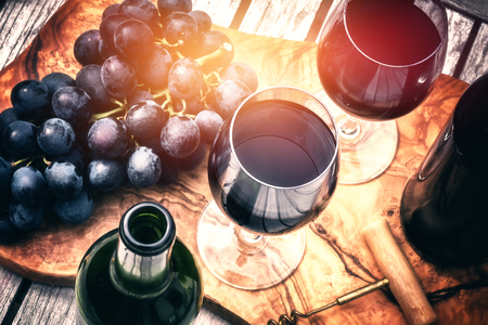 Setting with bottles of red wine, wine glasses and grapeの写真素材