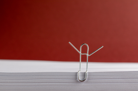 Paper Clip with Hands Aloft on White Paper on Red Backgroundの写真素材