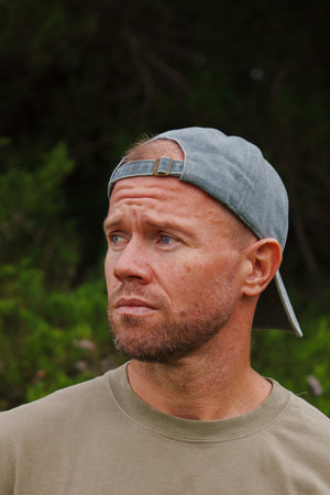 middle-aged muscular, blond, sporty man with a short beard, wearing a baseball cap, green T-shirt,...