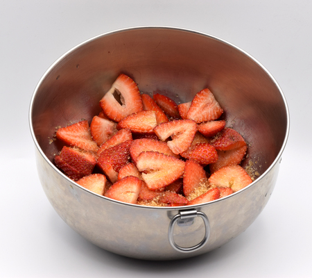 Cut strawberries in a metal bowl on a white backgroundの写真素材