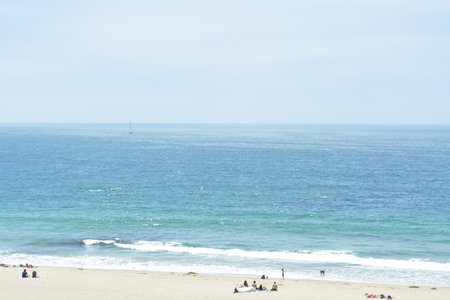 Calm Beach Scene With Gentle Waves and Distant Sailboat Under a Clear Sky in Midday Sunlightの写真素材