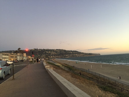 Evening Stroll Along the Quiet Beach Pathway as the Sun Sets Over the Ocean Waves and the Coastal Hillsの写真素材