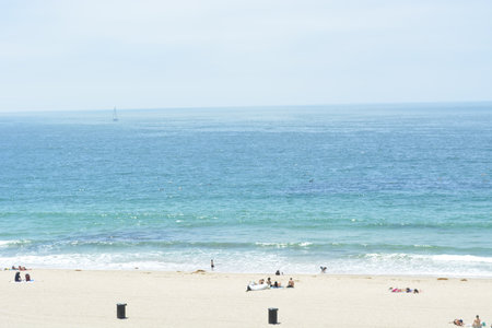 Coastal Serenity Captured on a Sunny Day at the Beach With Gentle Waves and Relaxed Visitors Enjoying Natureâs Beautyの写真素材