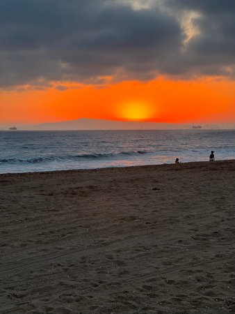 Golden Sunset Casts Vibrant Hues Over Tranquil Beach as Waves Gently Lap at the Shoreの写真素材