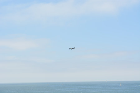 A Small Airplane Soars Through a Clear Blue Sky Over the Tranquil Ocean on a Sunny Afternoon Near the Coastlineの写真素材