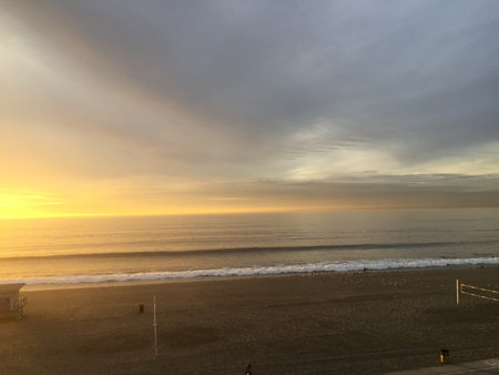 Majestic Sunset Over Calm Ocean Waves With Sandy Beach in the Foreground During Early Eveningの写真素材