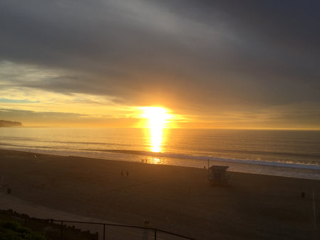 Sunset View Over a Serene Beach With Calm Waves and Distant Silhouettes of People Enjoying the Momentの写真素材