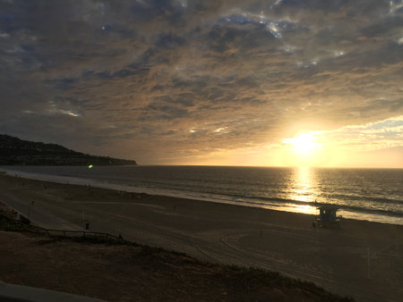 Sunset Over the Tranquil Beach With Gentle Waves and a Serene Lifeguard Tower in the Distanceの写真素材