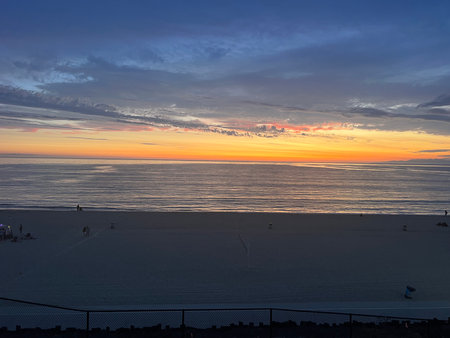 Vibrant Sunset Over a Tranquil Beach With Scattered People Enjoying the Serene Evening Atmosphereの写真素材