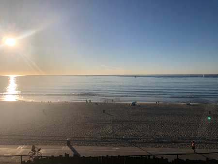 Evening Sunlight Dances on Calm Ocean Waves as Beachgoers Enjoy a Tranquil Seaside Retreatの写真素材