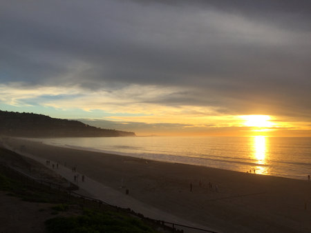 Sunset Reflects on Ocean Waves as Beachgoers Stroll Along the Shore at Dusk in a Serene Coastal Settingの写真素材