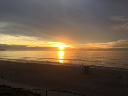 Golden Sunset Casts a Warm Glow Over Calm Ocean Waves at a Quiet Beach in the Early Evening Skyの写真素材