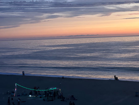 Serenity at Dusk as Beachgoers Enjoy a Vibrant Sunset Over Calm Watersの写真素材