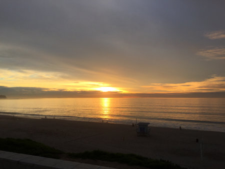 Golden Sunset Over Calm Ocean Waters With Soft Waves Gently Lapping the Shore and Silhouettes of People Enjoying the Eveningの写真素材