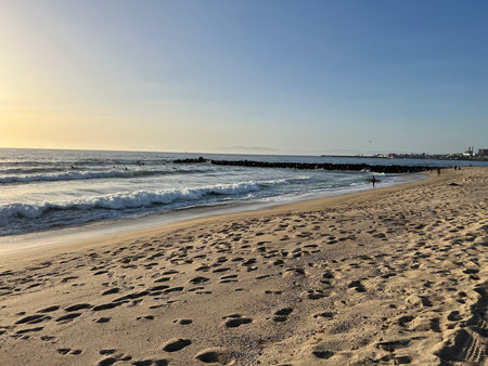 Golden Sunset Over a Tranquil Beach With Gentle Waves and Footprints in the Sandの写真素材