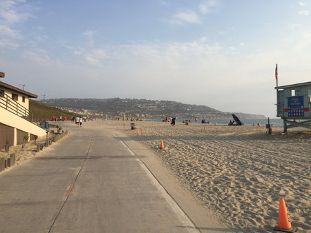People Enjoy a Peaceful Evening Stroll Along the Sandy Beach Under a Soft Sunset Sky Near a Coastal Townの写真素材