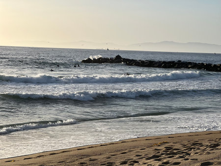 Waves Crash Gently on the Shore While Surfers Enjoy the Sunset at a Tranquil Beachの写真素材
