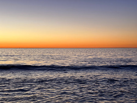 Serene Ocean Sunset Casting Warm Hues Over Gentle Waves and Distant Horizon at Twilightの写真素材