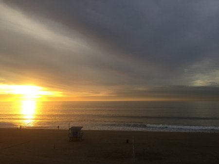 Golden Sunrise Casts Warm Light Over Calm Ocean Waves at Dawn by the Beachの写真素材