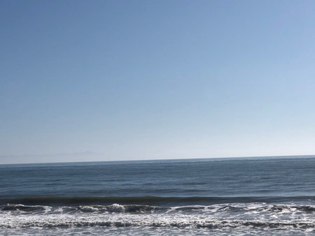 Calm Ocean Waves Gently Lapping at a Serene Shoreline on a Sunny Day Under a Clear Blue Skyの写真素材