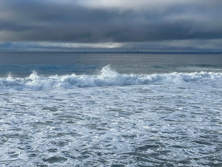 Ocean Waves Crash Gently on a Quiet Shore Under a Moody Sky at Dawnの写真素材