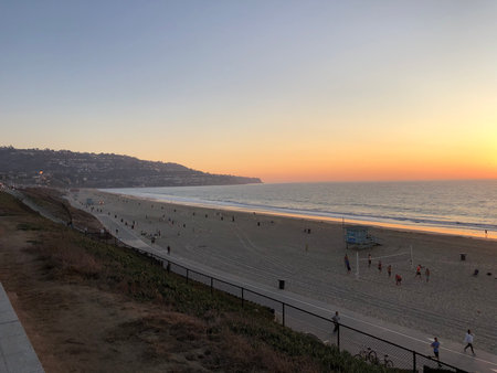 Vibrant Sunset Over the Sandy Beach, With Visitors Enjoying Evening Strolls and Playful Activities by the Shoreの写真素材
