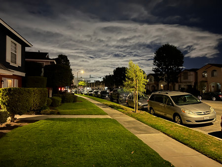 Quiet Neighborhood Street Illuminated by Moonlight Under a Beautiful Cloud-Filled Night Skyの写真素材