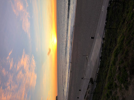 Vibrant Sunset Paints the Sky Over Tranquil Beach in Early Evening Glowの写真素材