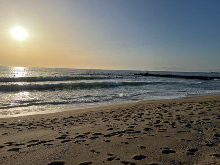 Sunset Casts a Golden Glow Over the Tranquil Beach With Gentle Waves and Footprints in the Sandの写真素材