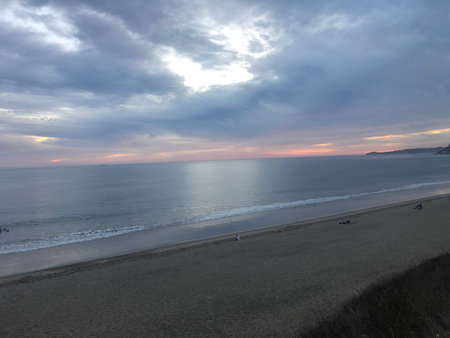 Peaceful Sunset Over a Calm Beach With Gentle Waves and Distant Silhouettes in the Evening Lightの写真素材