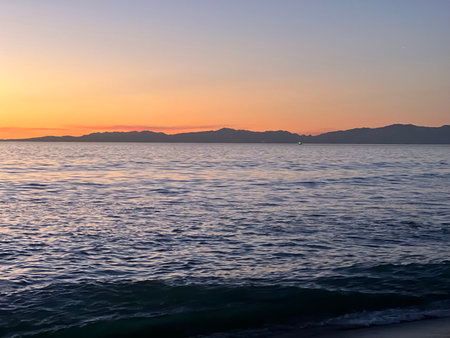 Evening Calm of the Ocean Reflects Twilight Hues Over Distant Mountains by the Shorelineの写真素材