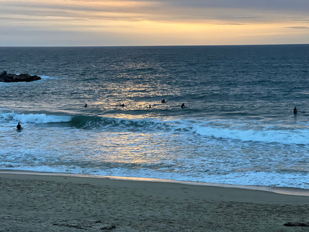 Surfers Enjoying Golden Hour Waves at the Beach Under a Vibrant Sunset Skyの写真素材