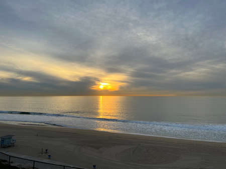 Serene Sunset Over the Tranquil Beach With Gentle Waves and Soft Clouds in the Sky During Early Eveningの写真素材