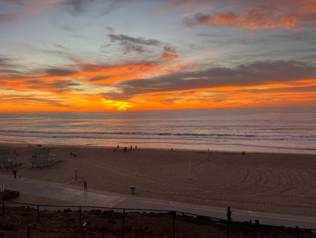 Vibrant Sunset Over a Serene Beach With Soft Waves and Silhouettes of People Enjoying the Eveningの写真素材