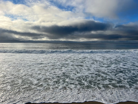 Waves Crashing Gently on a Serene Beach Under a Moody Sky During Twilight Hoursの写真素材