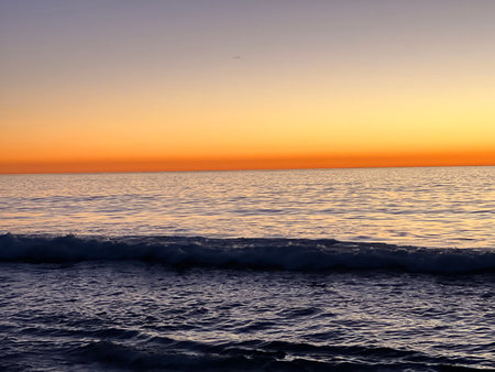 Sunset Over Calm Ocean Waves Reflecting Vibrant Orange and Purple Hues at the Beachの写真素材