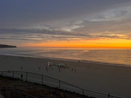 Sunset Casts a Warm Glow Over the Quiet Beach, as Families Enjoy Their Evening Stroll Along the Shorelineの写真素材