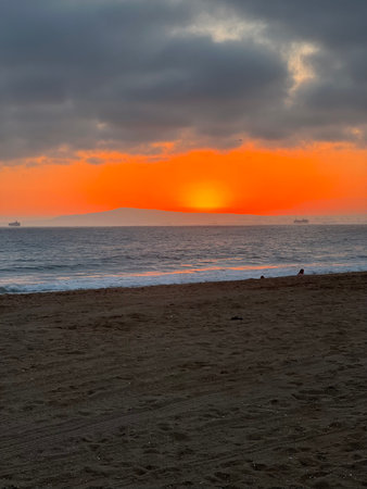 Vibrant Sunset Over the Ocean With Soft Waves and Distant Ships Creating a Serene Beach Atmosphereの写真素材