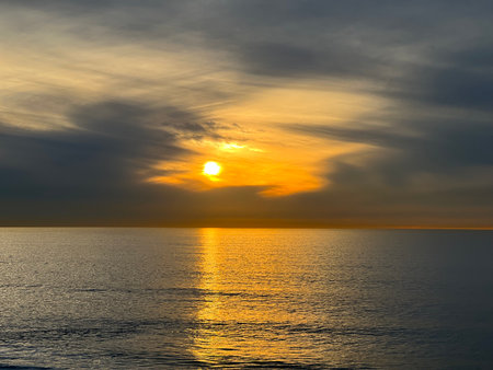 Bright Sunset Reflects on Calm Ocean Water With Soft Clouds During Late Afternoonの写真素材