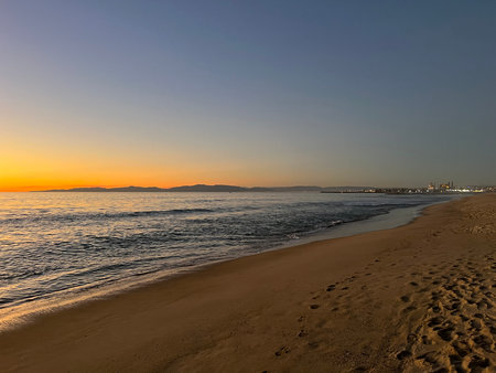 Stunning Sunset at the Beach With Waves Lapping Gently on the Shore and Distant Mountains Fading Into Twilightの写真素材