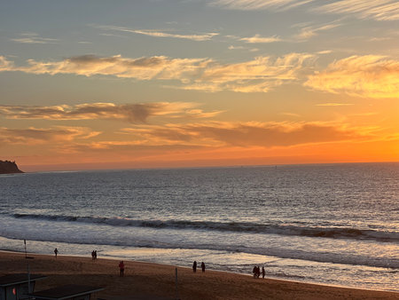 Sunset Over the Ocean With Silhouettes of People Strolling Along the Shoreline at a Tranquil Beachの写真素材