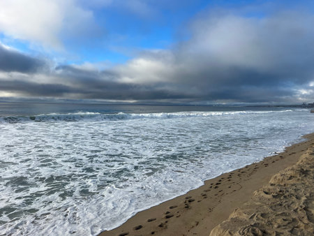 Gentle Waves Lap Against a Sandy Shore Under a Partly Cloudy Sky at Dawnの写真素材