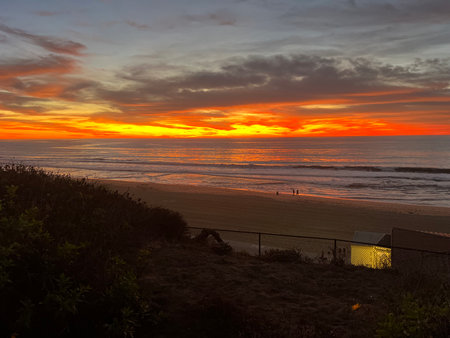 Sunset Hues Dance Across the Ocean Waves While Beachgoers Enjoy the Serene Coastline Under a Vibrant Skyの写真素材