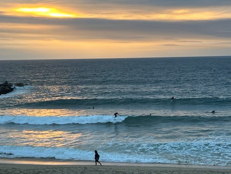 Surfers Ride Gentle Waves as the Sun Sets Over the Tranquil Beach in the Early Eveningの写真素材