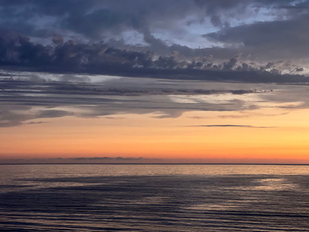 Vibrant Sunset Casts Colorful Reflections Across Calm Ocean Waters Near Distant Mountainsの写真素材