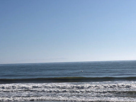 Calm Ocean Waves Gently Lap at the Shore Under a Clear Blue Sky on a Sunny Dayの写真素材