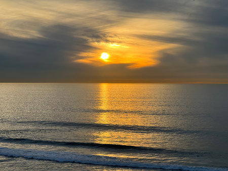 Golden Sunset Over Calm Ocean Waters Reflecting Warm Hues and Gentle Waves in Serene Coastal Setting During Evening Hoursの写真素材