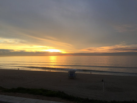 Sunset Over the Calm Beach at Golden Hour With Silhouettes of People Enjoying the Serene Atmosphere and Wavesの写真素材