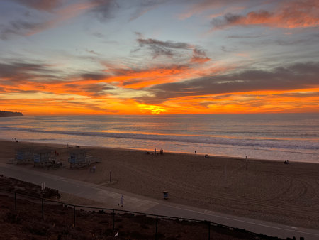 Majestic Sunset Over the Ocean With Vibrant Colors Illuminating the Beach and Silhouettes of People Enjoying the Eveningの写真素材