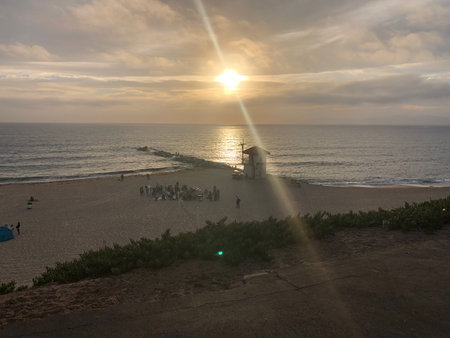 People Gather on the Beach at Sunset Near a Lifeguard Tower, Enjoying a Peaceful Evening by the Oceanの写真素材